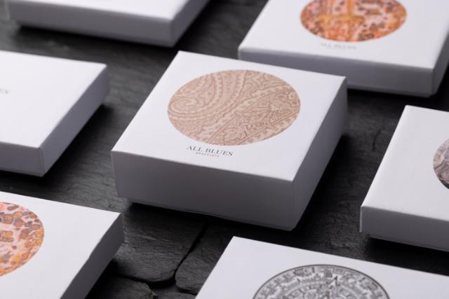 Ein grauer Deckel einer Schachtel mit einem aufwendigen kreisförmigen Muster und der Aufschrift