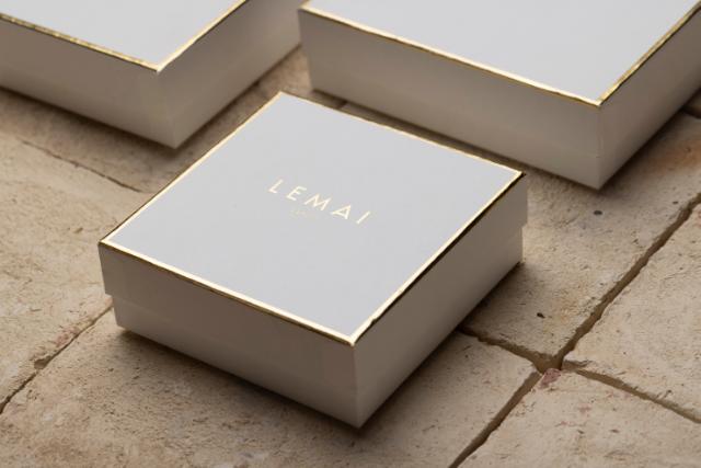 Drei quadratische, harte Schachteln mit goldener Heißfolienprägung des Logos