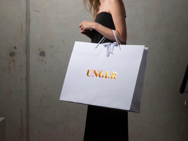 Rau hält eine UNCLR-Tasche in Weiß mit goldener Schrift.